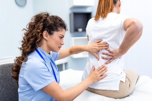 Healthcare professional examining woman’s lower back while seated on medical exam table