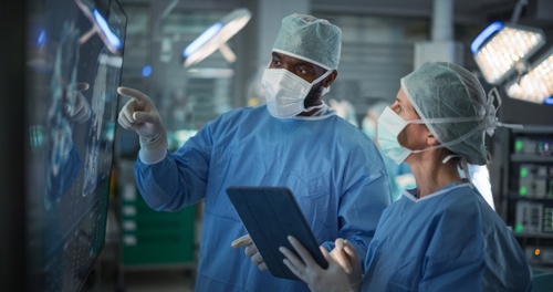 Surgeons in operating room reviewing brain scan on monitor with tablet