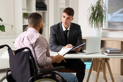 Lawyer working beside man in wheelchair at office desk with documents