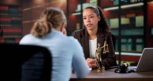 female attorney consulting client across desk with Lady Justice statue and gavel